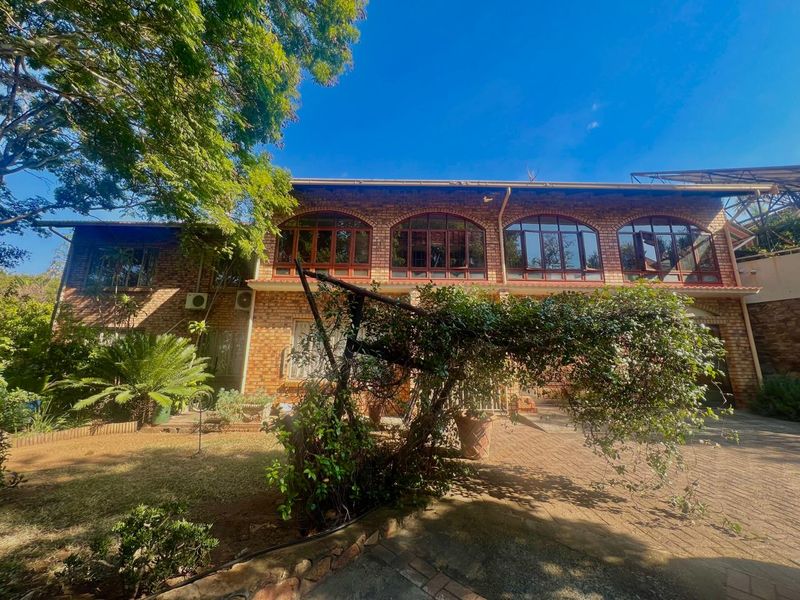 Rear view of a face brick house featuring arched timber windows, a paved patio area, and established garden surroundings.