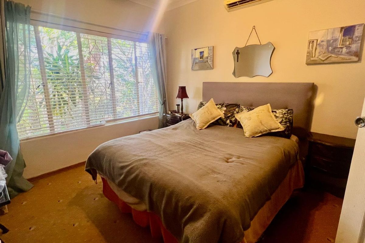 A bedroom featuring a large window with security bars, carpet flooring, and a wall-mounted split-system air conditioner.