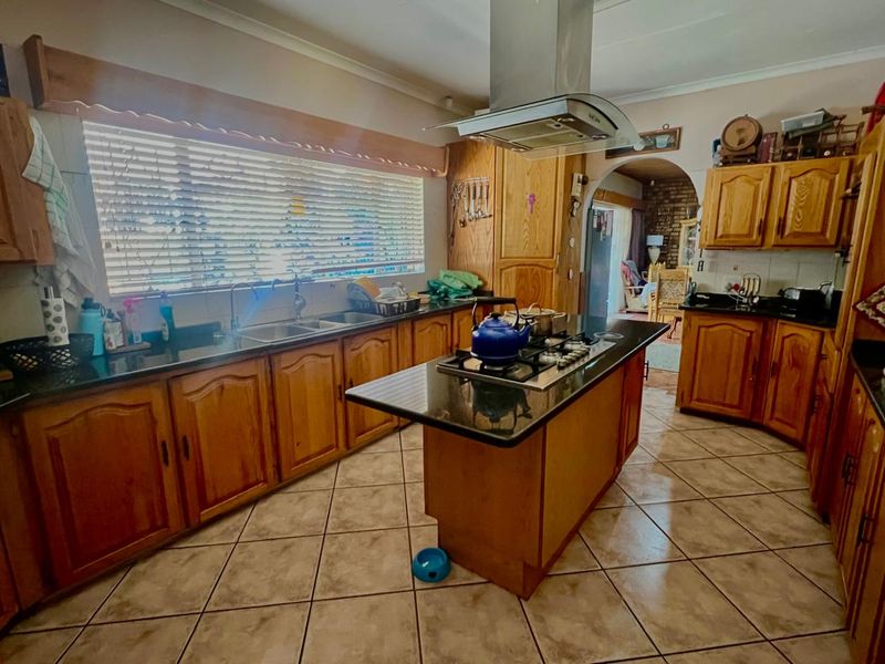 A traditional kitchen featuring wooden cabinetry, granite countertops, a central island with a gas hob, and tiled flooring.