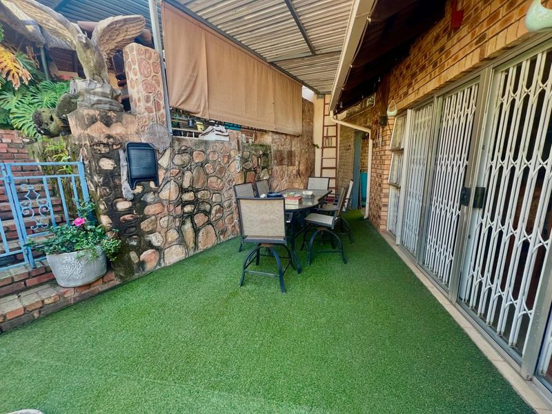 Covered outdoor patio area featuring artificial turf, stone feature walls, and direct access to the home through sliding security doors.