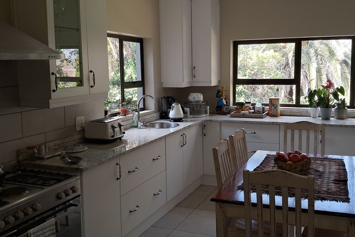 A well-maintained kitchen featuring white cabinetry, granite countertops, a gas hob with extractor fan, and large windows providing natural light and garden views.