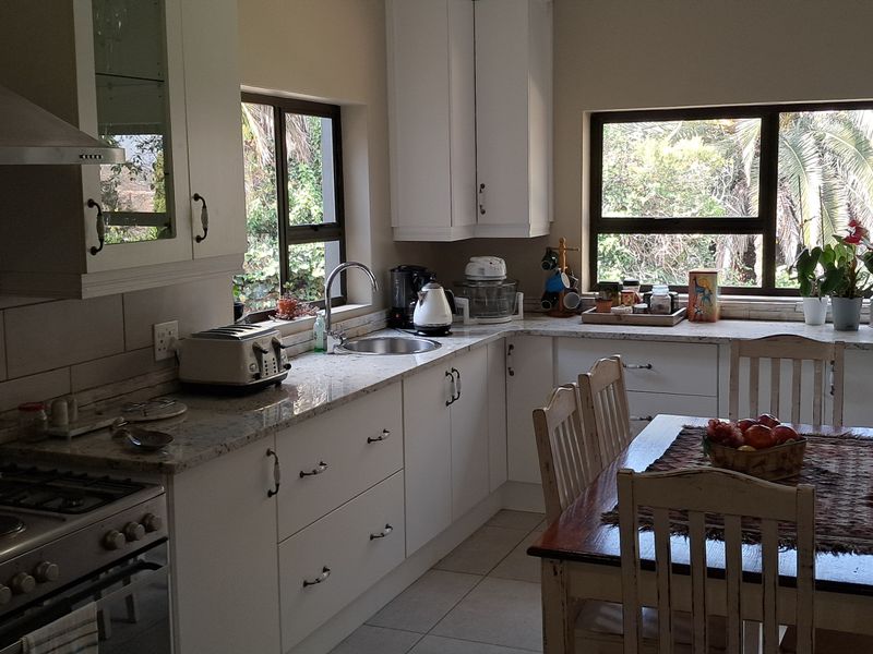 A well-maintained kitchen featuring white cabinetry, granite countertops, a gas hob with extractor fan, and large windows providing natural light and garden views.