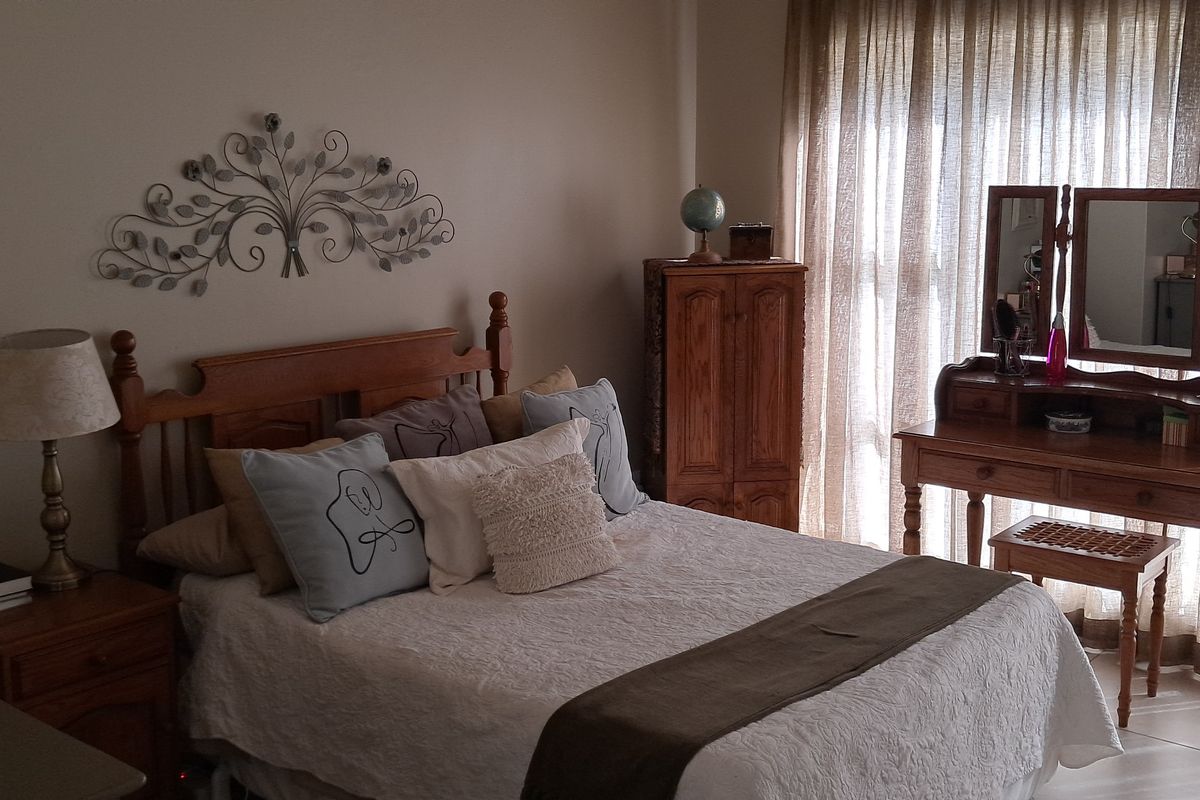 A well-lit bedroom featuring tiled flooring and large windows with floor-to-ceiling curtains, providing a comfortable and functional living space.