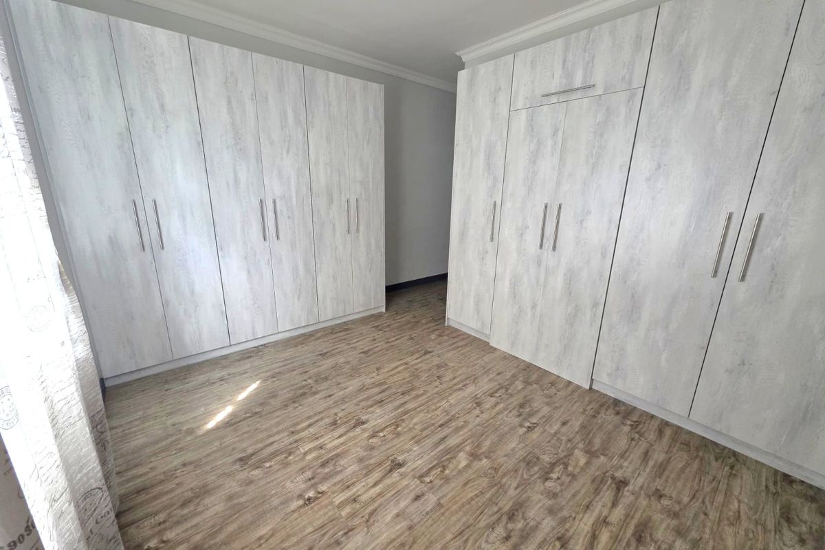 A bright bedroom featuring extensive built-in cabinetry with a light wood-grain finish and modern laminate flooring.