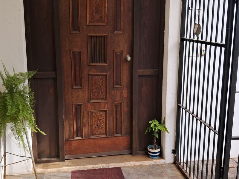 A secure entrance area featuring a solid timber front door, tiled flooring, and a protective metal security gate.