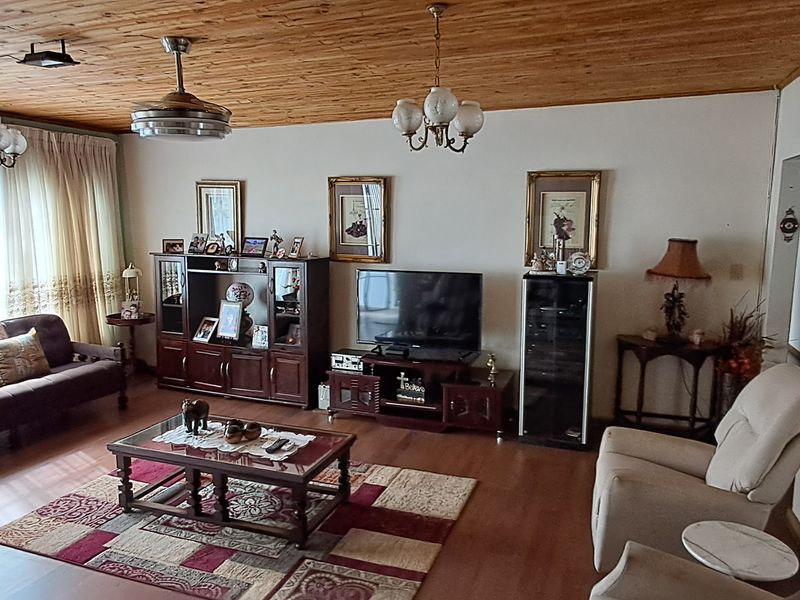 A spacious living room featuring a warm timber-clad ceiling, laminate flooring, and classic lighting fixtures, offering a comfortable and traditional living environment.