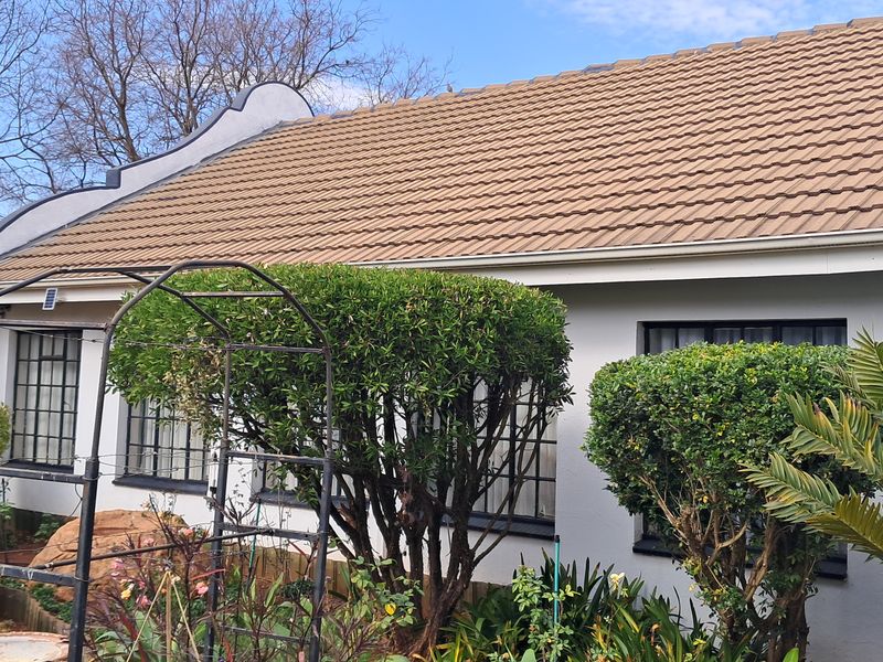 A well-maintained rear exterior view of the house featuring a tiled roof, metal-framed windows, and a landscaped garden area.