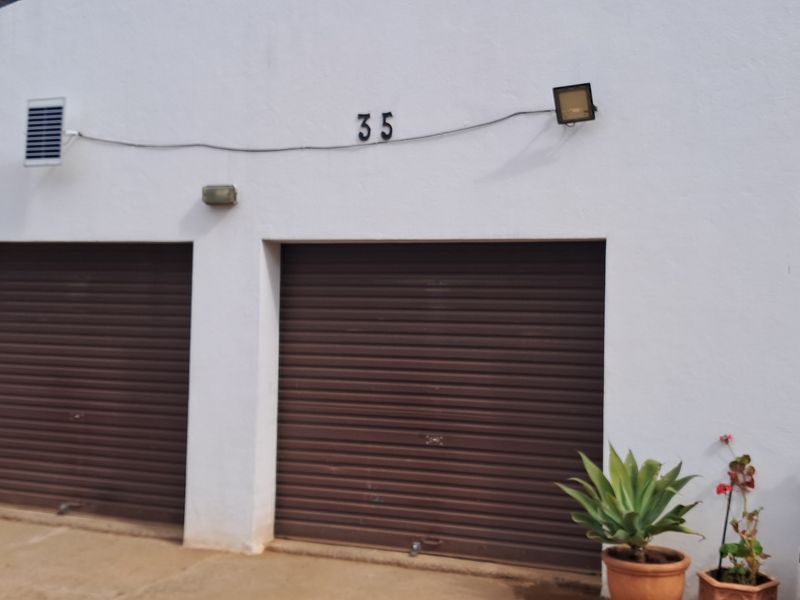 A double garage facade featuring brown roller doors and exterior lighting, with visible house numbering on the white rendered wall.