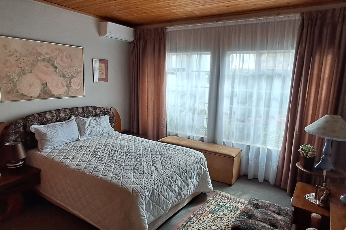 A cozy bedroom featuring a timber-paneled ceiling, a wall-mounted air conditioning unit, and large windows that allow for natural light.