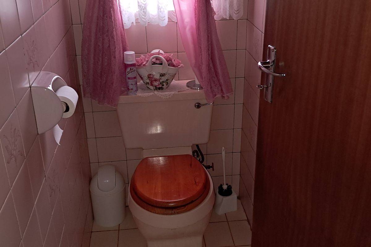 A compact bathroom featuring dated pink wall tiles and matching floor tiles, equipped with a standard toilet suite.