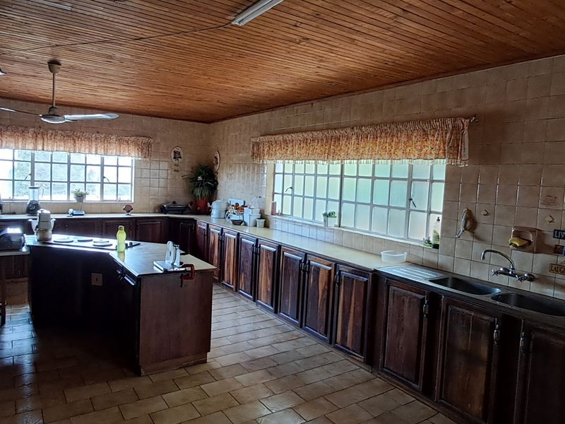 Spacious kitchen featuring extensive wooden cabinetry, tiled countertops, double basin sink, and a traditional wooden ceiling with a ceiling fan.
