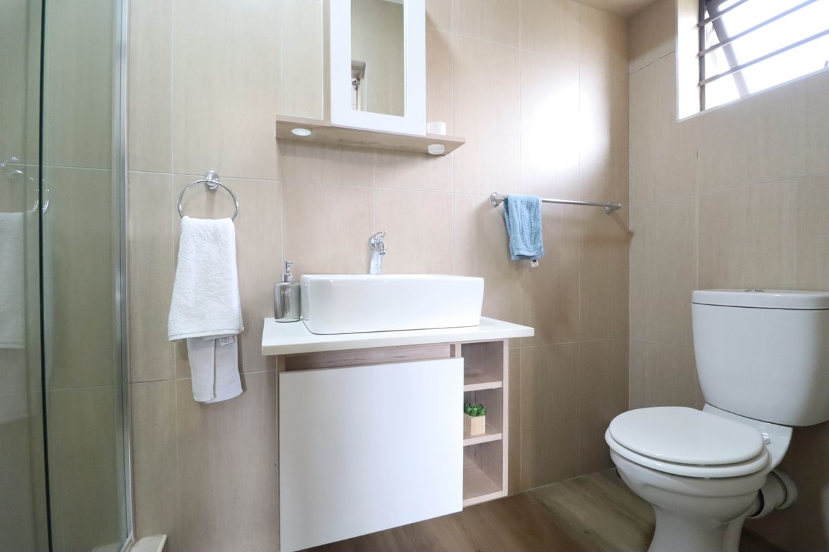 Modern bathroom featuring a vessel sink vanity, medicine cabinet, toilet, and a glass-enclosed shower with neutral wall tiling.