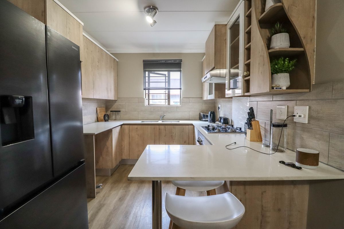 Modern kitchen featuring light wood-look cabinetry, stone countertops, a gas hob with extractor, and a functional breakfast bar layout.