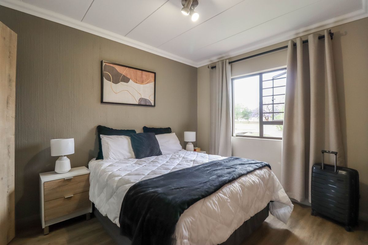 A well-maintained bedroom featuring laminate flooring, a built-in wardrobe, and a window fitted with security bars for added peace of mind.