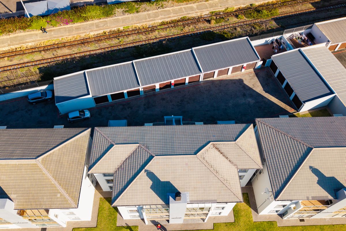 Aerial view of the apartment complex featuring multiple residential buildings with tiled roofs, a central paved driveway, and a dedicated garage block.