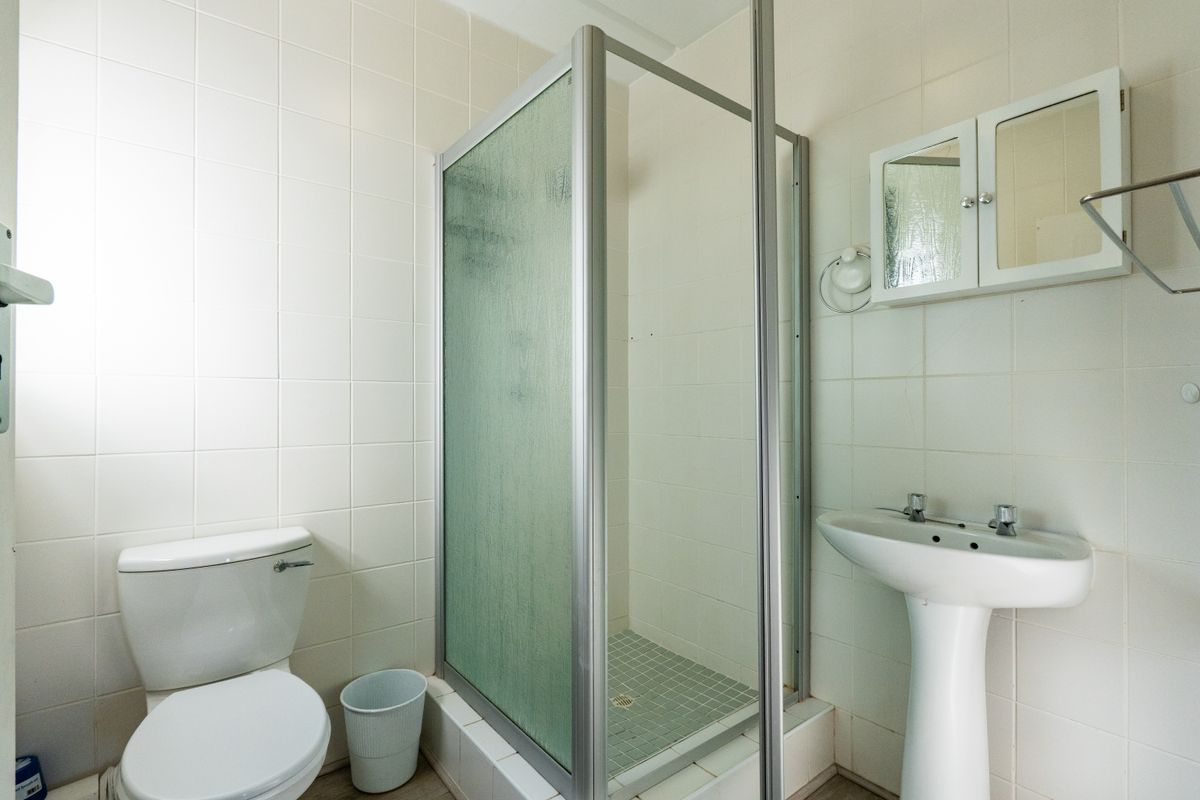 A functional bathroom featuring a shower enclosure, pedestal basin, and toilet, finished with white wall tiles and a wall-mounted medicine cabinet.