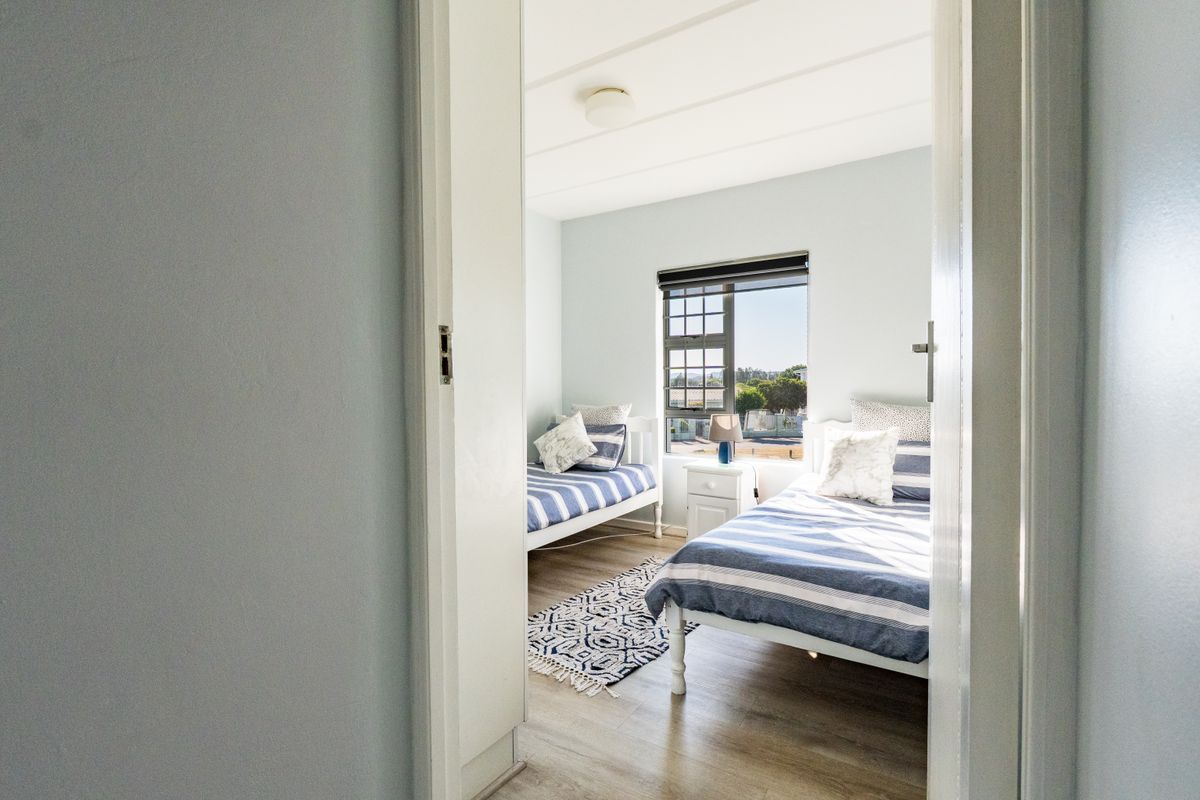 A bright bedroom featuring laminate flooring, a window with security bars, and a neutral color palette, viewed from the doorway.