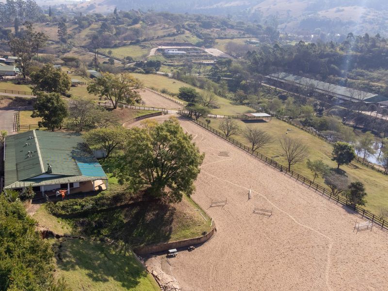 Aerial view of a farm property featuring an equestrian arena, fenced paddocks, and a main building with a green metal roof.