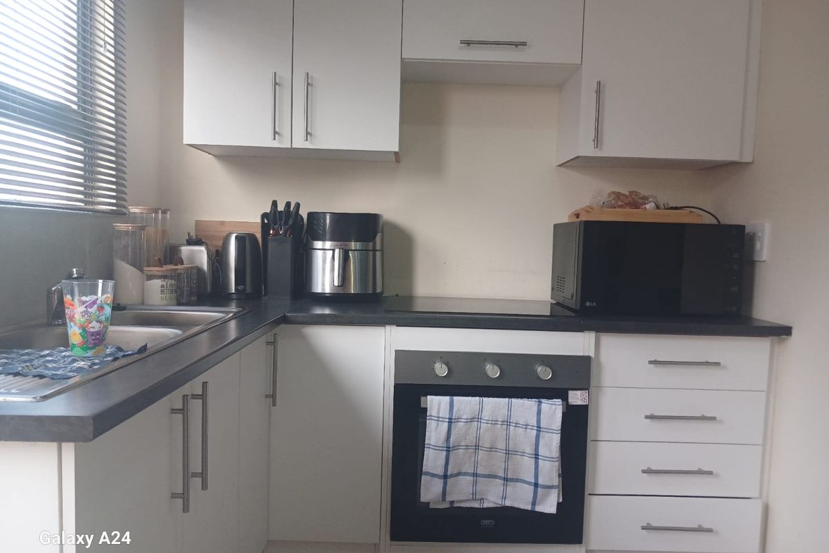 A compact kitchen featuring white cabinetry, dark laminate countertops, a built-in oven, and an electric cooktop.