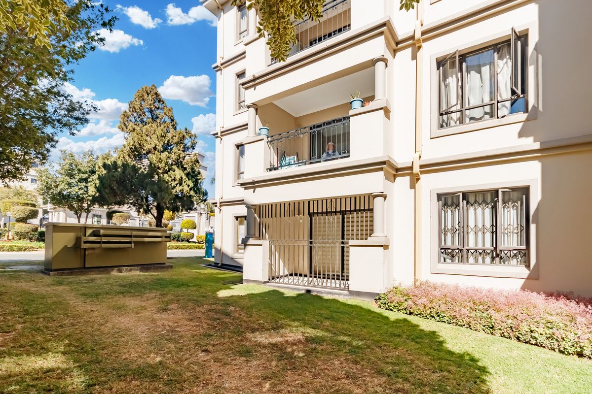 A view of the apartment building exterior featuring a ground floor patio with security gates and an upper-level balcony with metal railings.