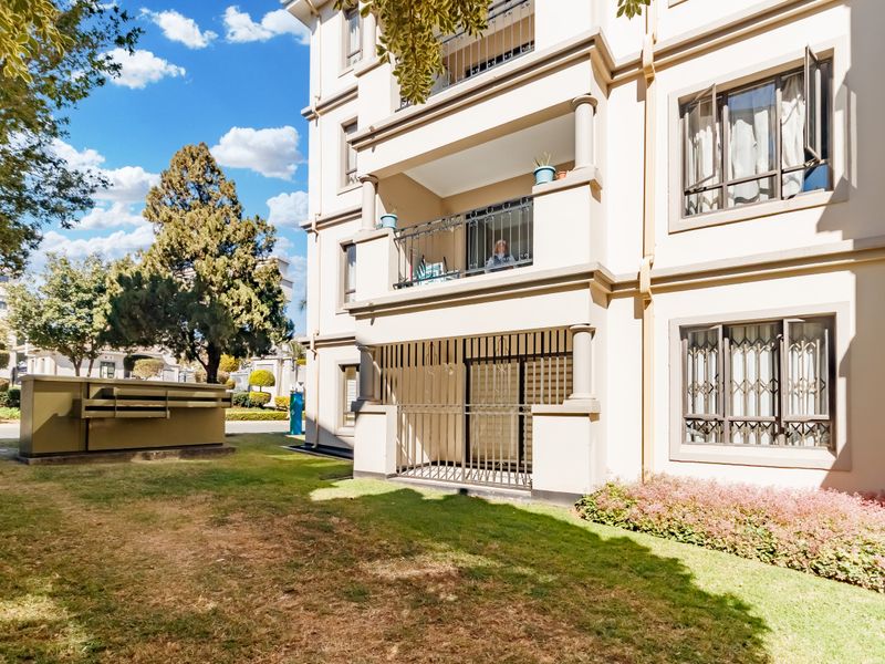 A view of the apartment building exterior featuring a ground floor patio with security gates and an upper-level balcony with metal railings.