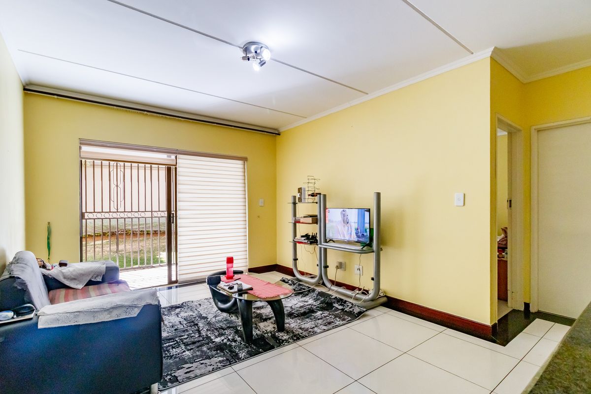 A living room featuring tiled flooring and a sliding glass door with an integrated security gate, providing access to the exterior.