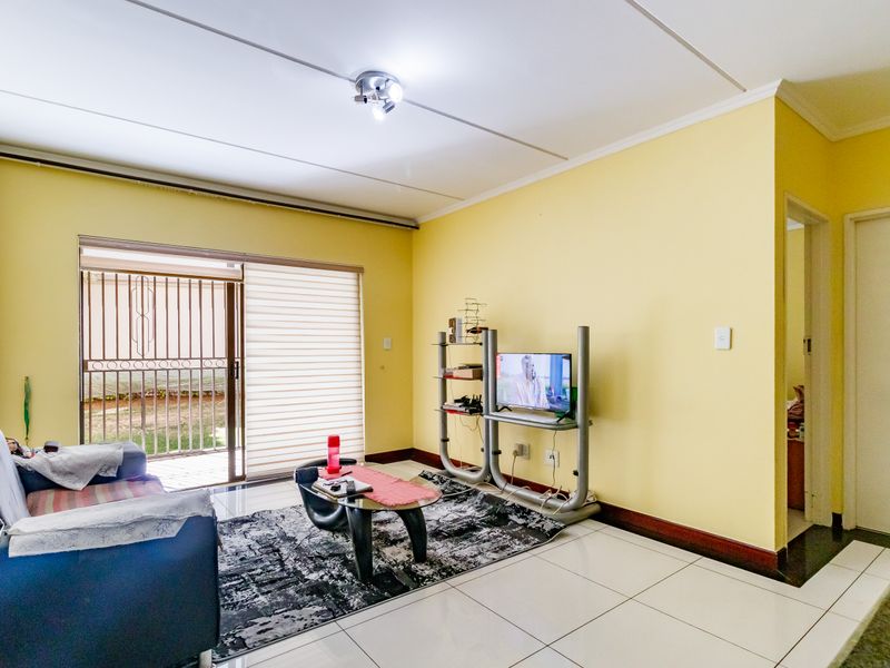 A living room featuring tiled flooring and a sliding glass door with an integrated security gate, providing access to the exterior.