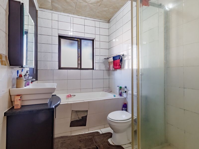 A functional bathroom featuring a bathtub, separate shower enclosure, toilet, and vanity basin with tiled finishes throughout.