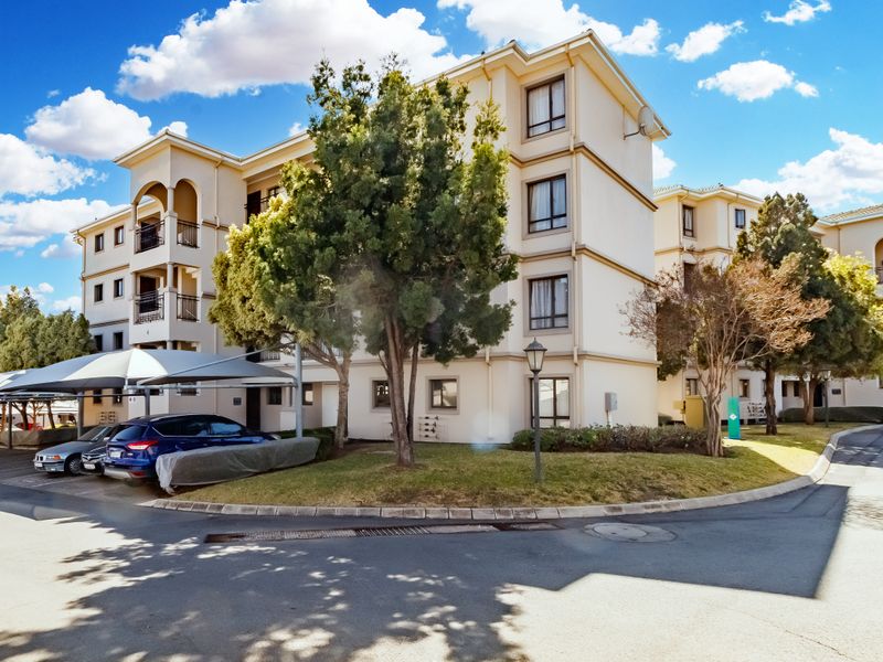 Exterior view of a multi-story apartment complex featuring covered parking bays, private balconies, and well-maintained landscaped grounds.