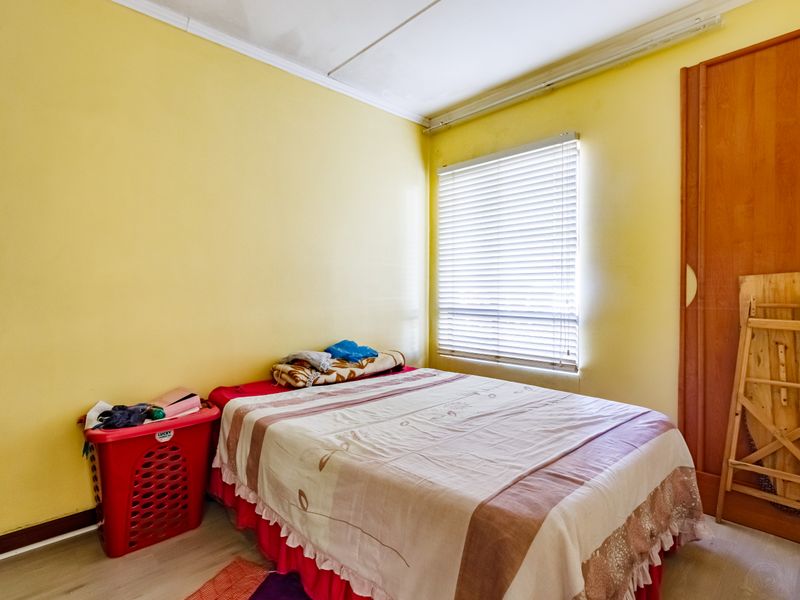 A bedroom featuring laminate flooring, a built-in wardrobe, and venetian blinds. The space would benefit from a fresh coat of paint and ceiling repairs.