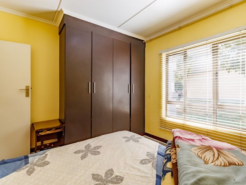 A bedroom featuring a dark built-in wardrobe, yellow walls, and a window fitted with venetian blinds.