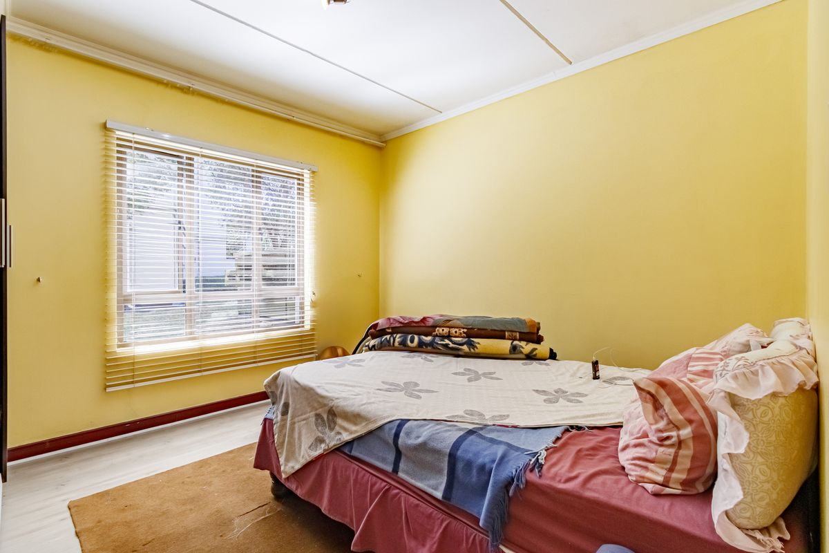 A bedroom featuring yellow walls, laminate flooring, and a window with venetian blinds. The room requires cosmetic updates to improve its overall condition.