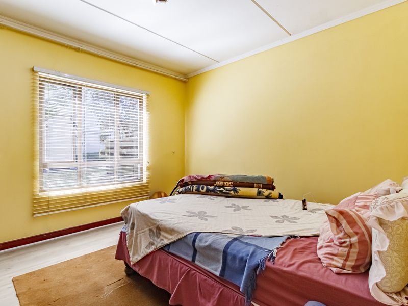 A bedroom featuring yellow walls, laminate flooring, and a window with venetian blinds. The room requires cosmetic updates to improve its overall condition.