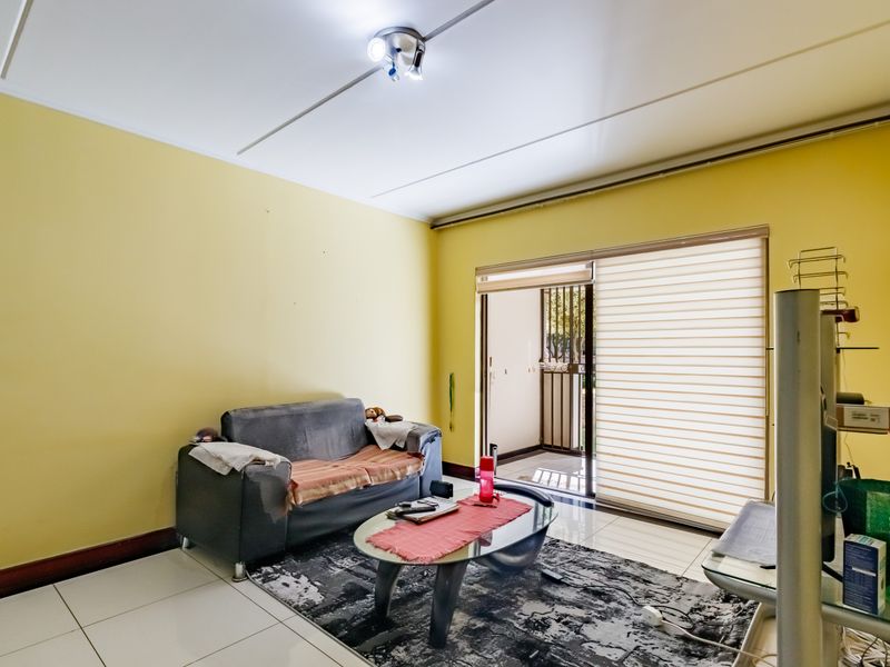 A living room featuring tiled flooring and a sliding glass door with roller blinds, providing access to an outdoor area.