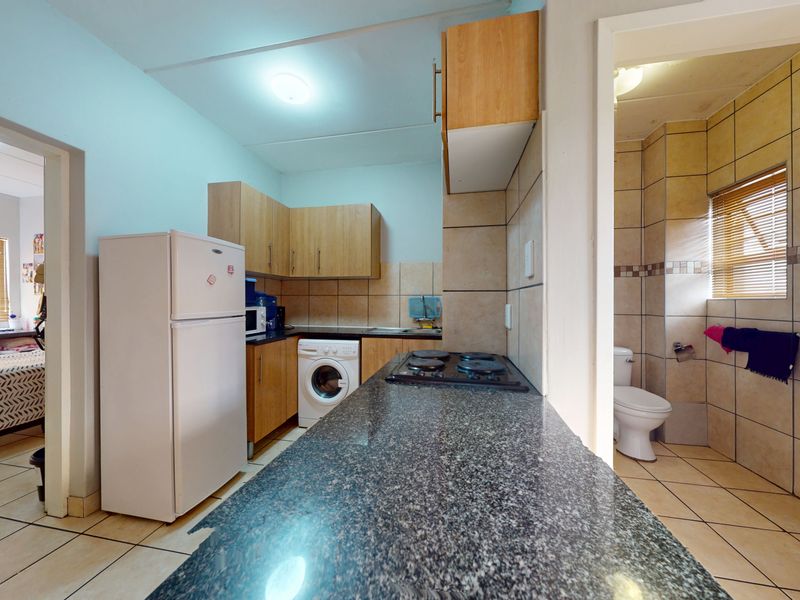 Compact kitchen featuring granite countertops, built-in cabinetry, and a hob, with adjacent access to a tiled bathroom and bedroom area.