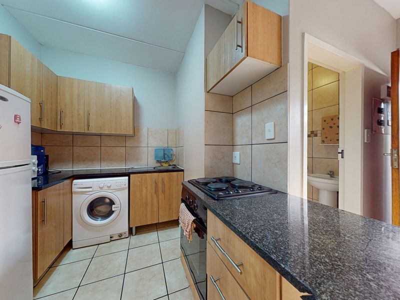 Functional kitchen featuring laminate cabinetry, granite countertops, built-in oven and hob, and tiled finishes, with direct access to an adjacent bathroom area.