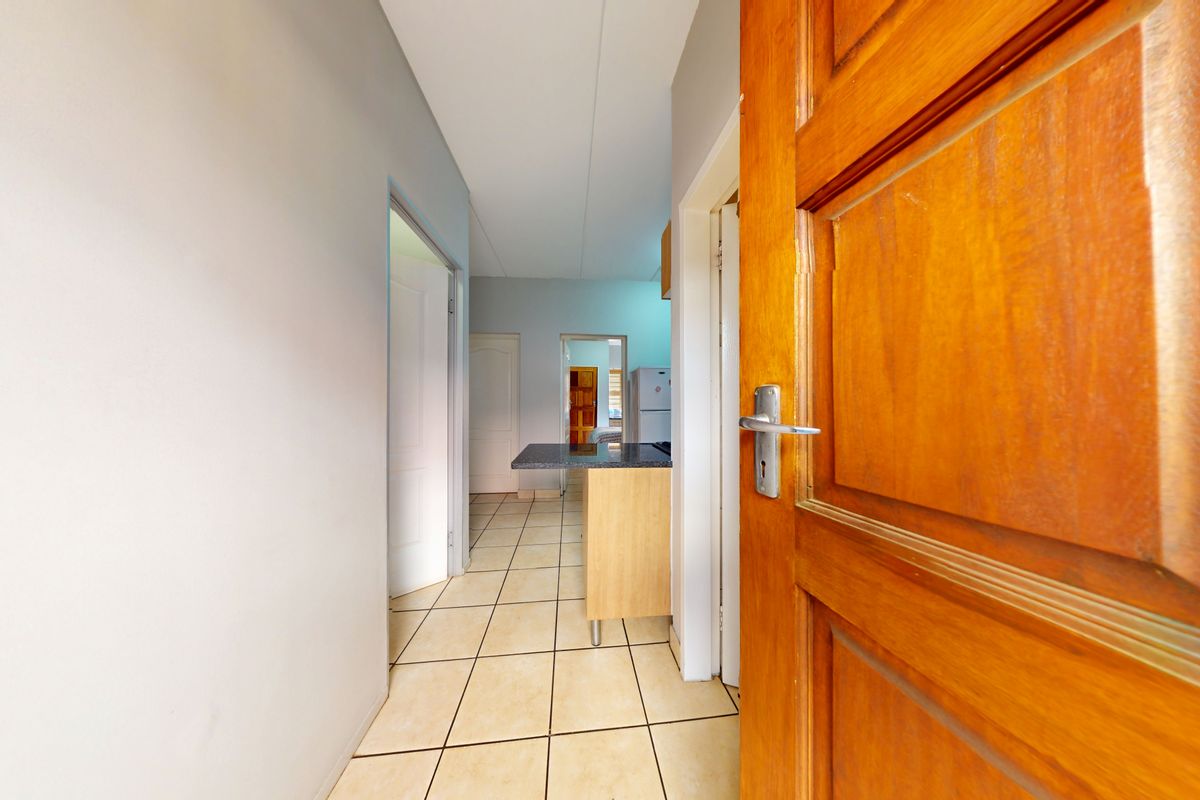 A view from a wooden doorway into a tiled hallway leading towards a kitchen area with granite countertops.