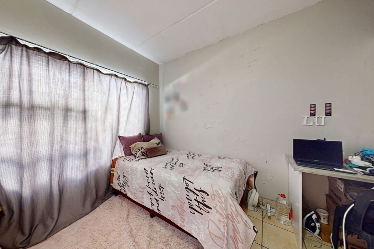 A bedroom featuring tiled flooring and a built-in desk, currently showing signs of wall surface wear and peeling paint.