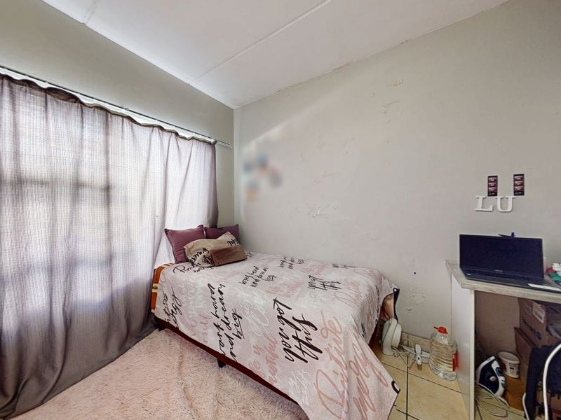 A bedroom featuring tiled flooring and a built-in desk, currently showing signs of wall surface wear and peeling paint.