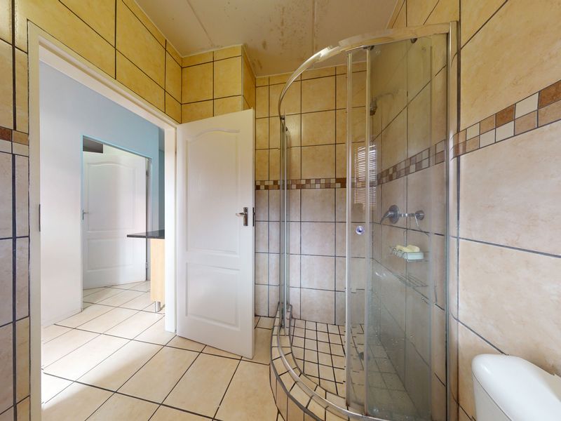 A dated bathroom featuring a curved glass shower enclosure and tiled finishes, showing signs of ceiling water damage and requiring cosmetic updates.
