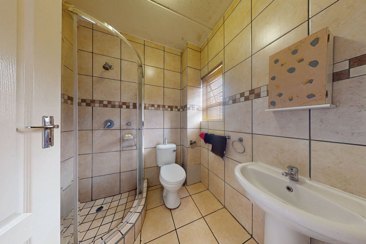 A compact bathroom featuring a curved glass shower enclosure, pedestal washbasin, and toilet, finished with neutral ceramic wall and floor tiling.