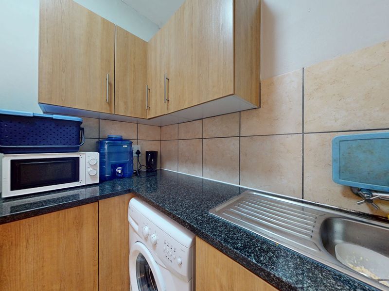 Compact scullery area featuring laminate cabinetry, granite countertops, a stainless steel sink, and dedicated space for laundry appliances.