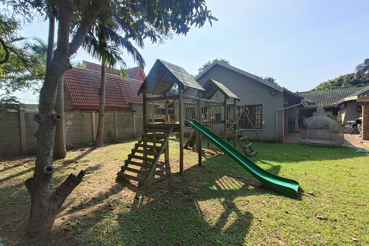 A spacious rear garden featuring a lawn, a timber jungle gym, and a paved patio area adjacent to the main house structure.