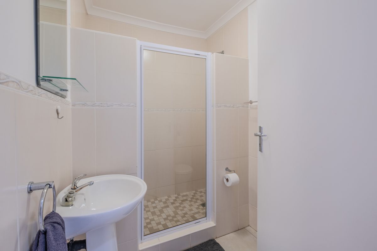 A functional bathroom featuring a pedestal basin, a glass-enclosed shower with mosaic floor tiling, and neutral wall tiles.