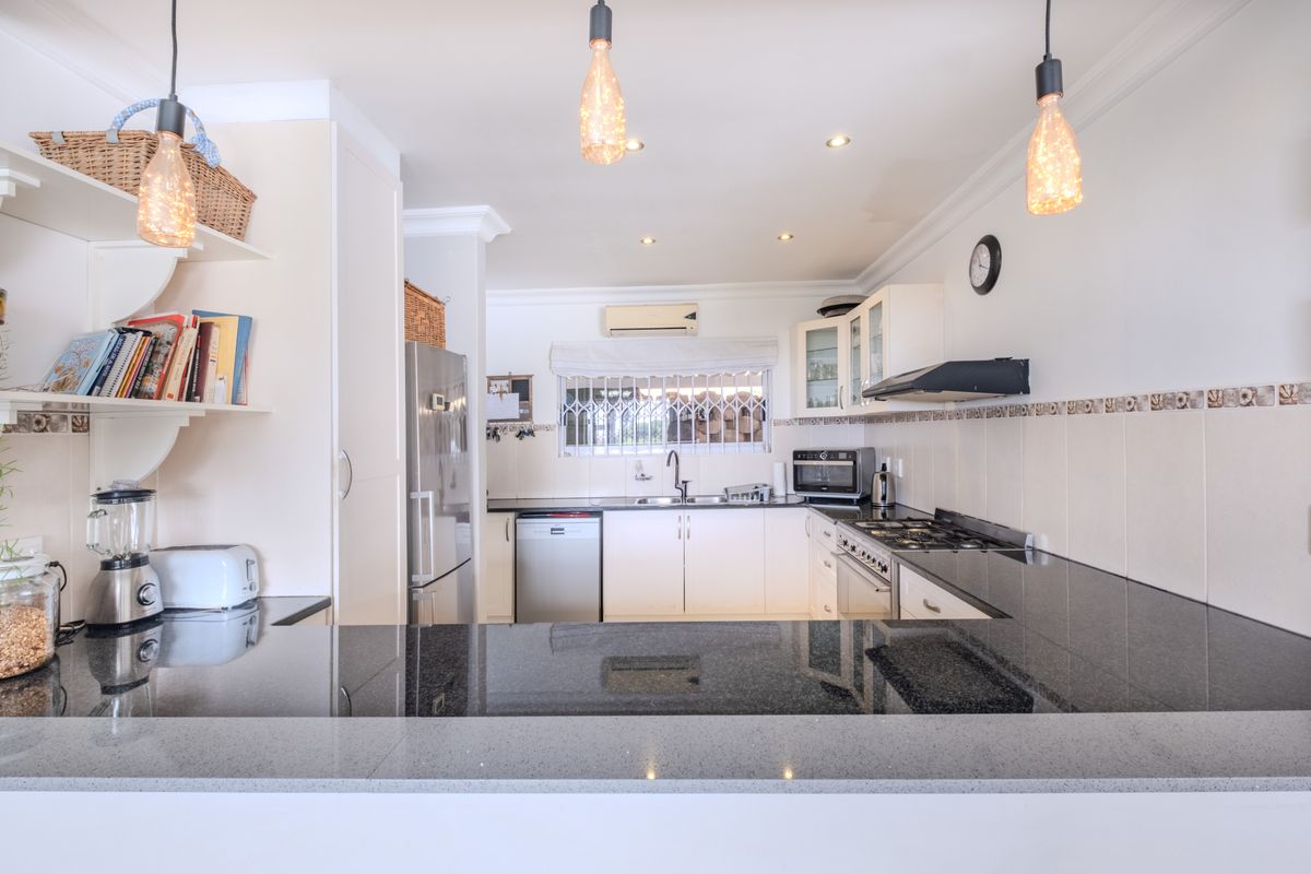 A well-maintained kitchen featuring granite countertops, built-in cabinetry, a gas hob with extractor fan, and a breakfast bar overlooking the space.