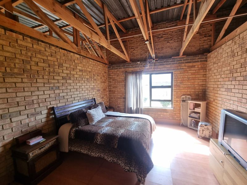 A rustic bedroom featuring exposed timber roof trusses and facebrick walls, offering a unique industrial aesthetic with potential for modern interior design updates.