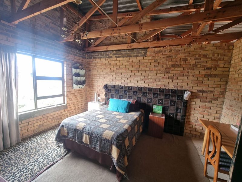 A rustic bedroom featuring exposed brick walls and timber roof trusses, offering a unique industrial aesthetic with potential for modern interior updates.