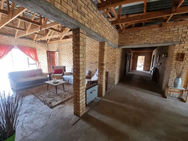 Open-plan living area featuring exposed brick walls, timber roof trusses, and concrete flooring, offering a rustic, industrial-style aesthetic with potential for further finishing.