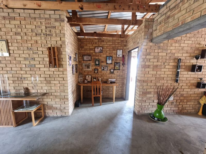 Rustic living area featuring exposed brick walls, concrete flooring, and an open timber truss ceiling, offering a raw industrial aesthetic.