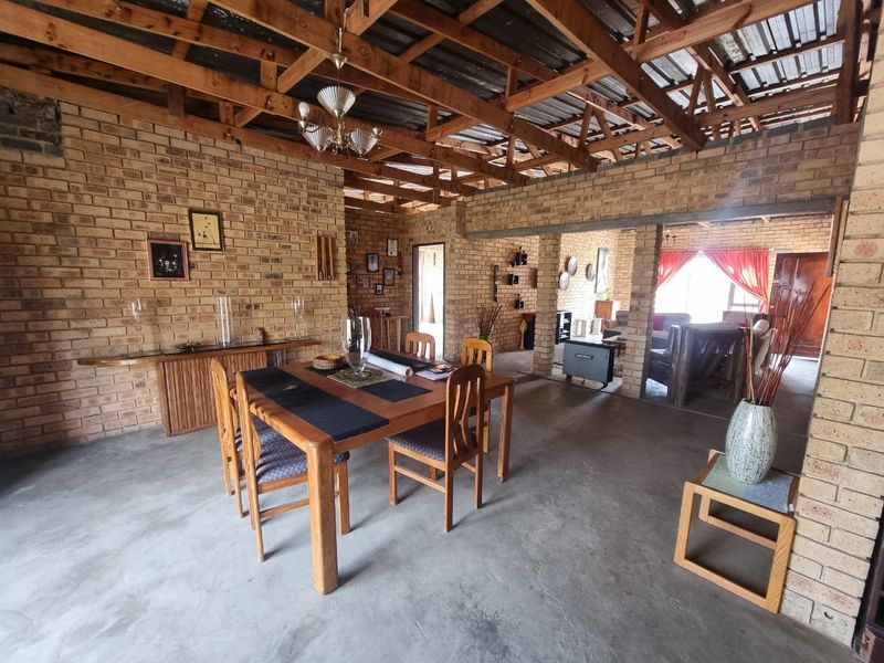 Spacious open-plan living and dining area featuring rustic facebrick walls, exposed timber roof trusses, and polished concrete flooring.